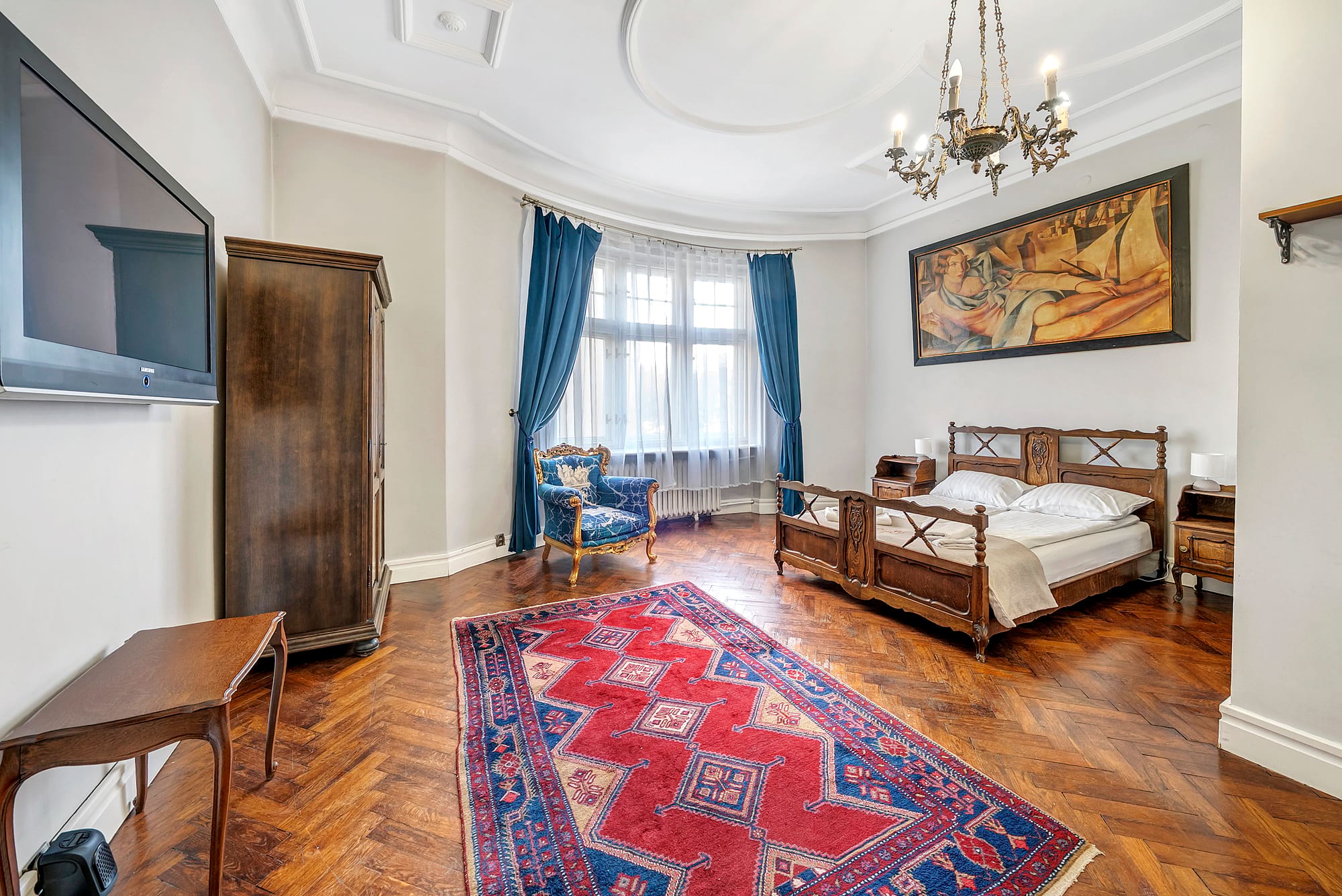 Elegancka sypialnia z drewnianym łączem łóżkiem, dużymi oknami z błękitnymi zasłonami i jasnym żyrandolem nad centrum