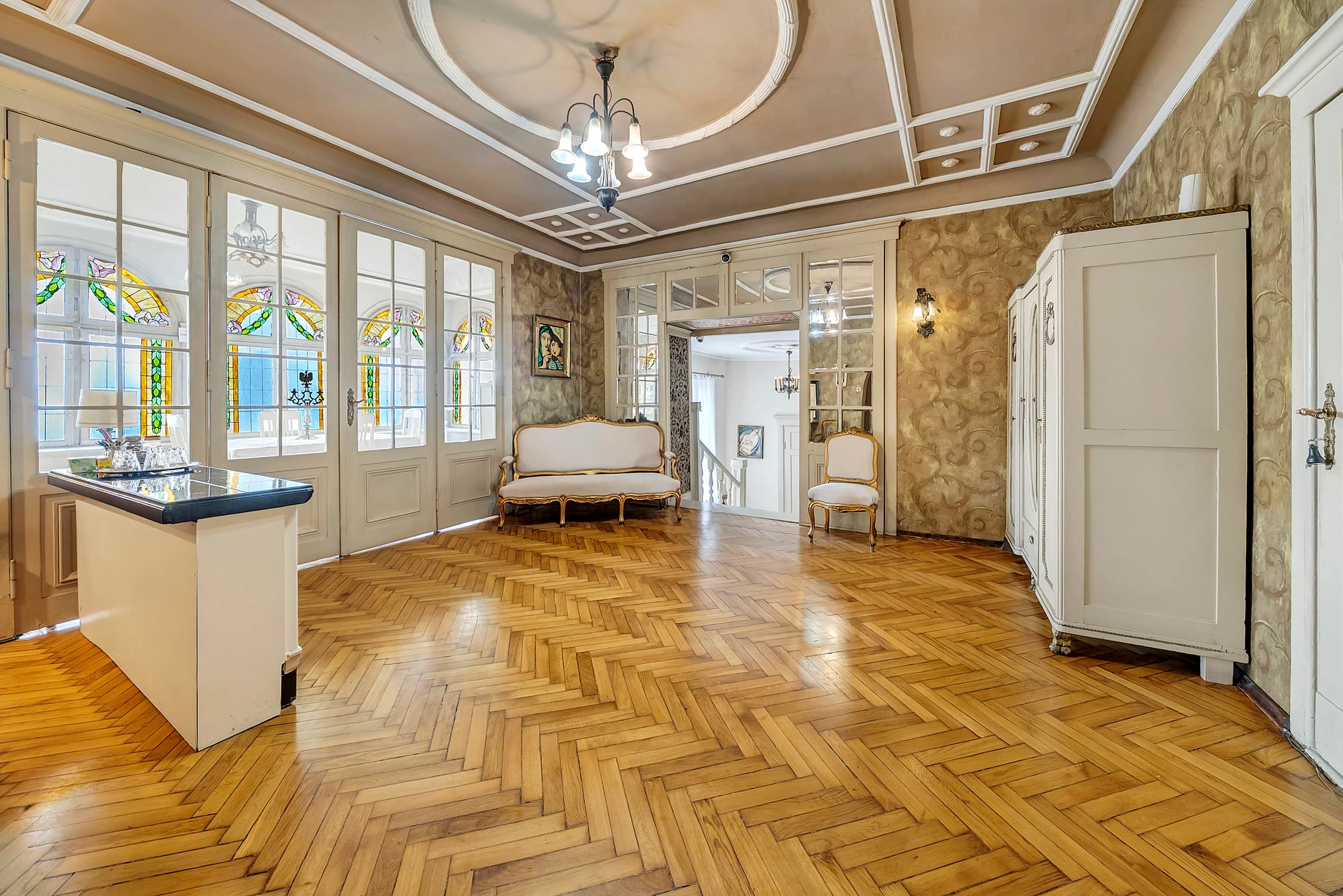 Elegancki salon z parkietem i zabytkowym wystrojem, jasne meble i witraże przy oknach